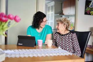 Medewerker Thuiszorg met bewoner en tabblad die een kopje koffie drinken en elkaar aankijken